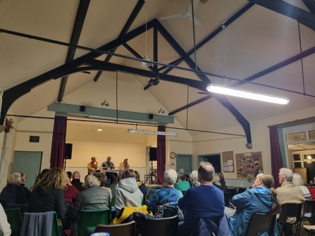 Audience looking over panel discussion on stage in village hall